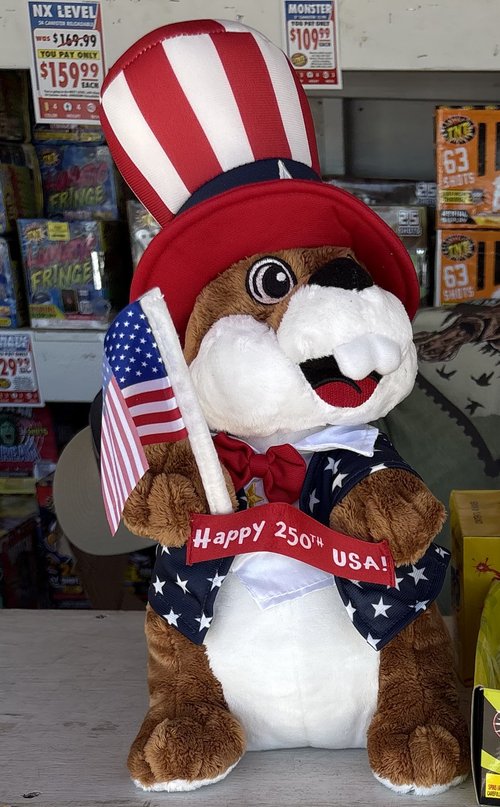 Plush Uncle Sam mascot with a Happy 250th USA banner at the fireworks stand